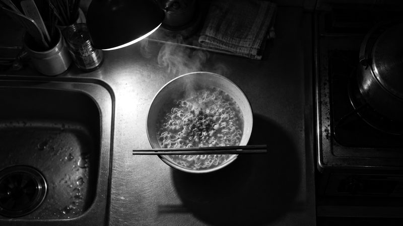 夜の台所で、お湯を注いだばかりのインスタントラーメンから湯気が立つ（イメージ）