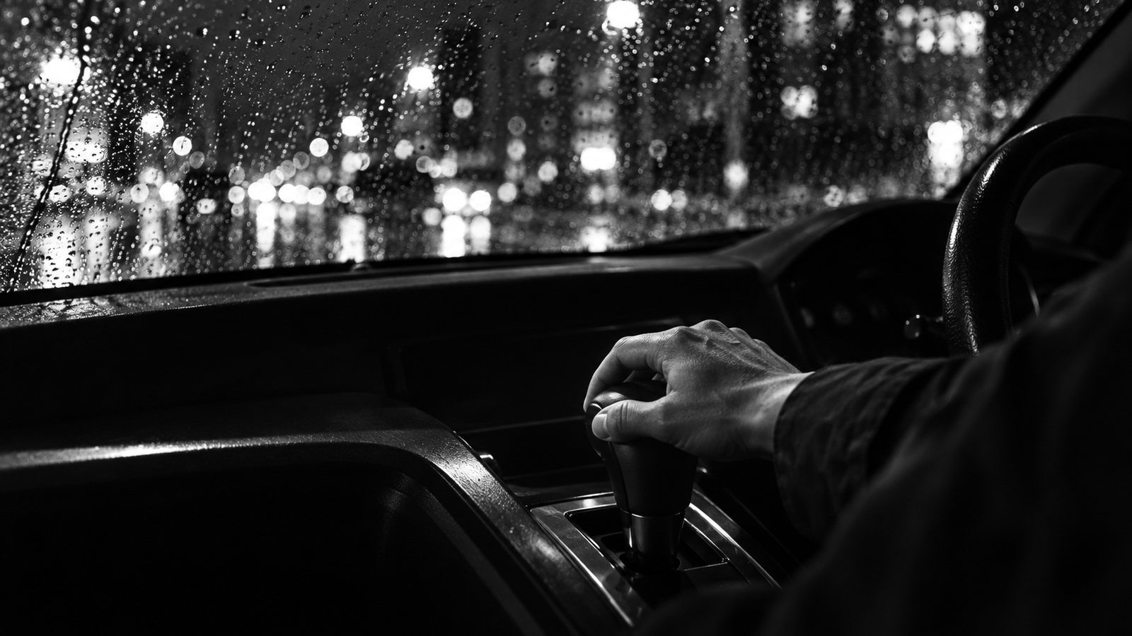 雨の夜、オートマ車のシフトレバーに手を置く運転席(イメージ)